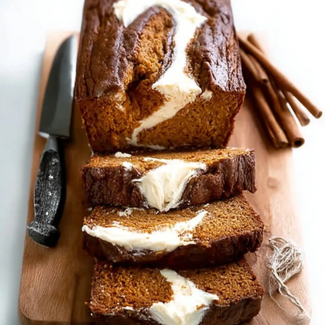 A moist pumpkin bread loaf with a rich cream cheese swirl, sliced to reveal its creamy center.