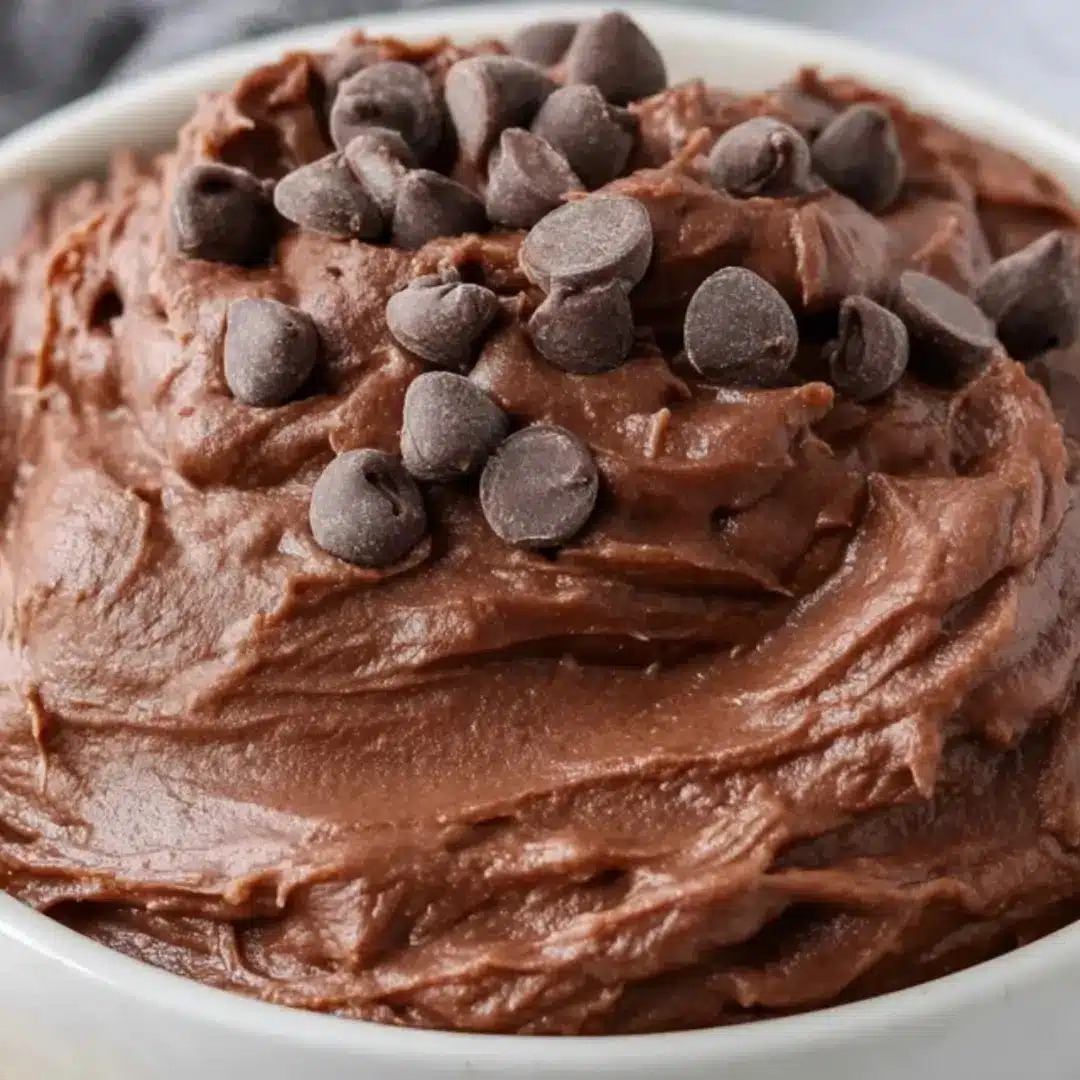 A close-up shot of a creamy chocolate Brownie Batter Dip in a white bowl, surrounded by fresh strawberries, graham crackers, and salty pretzels for dipping.