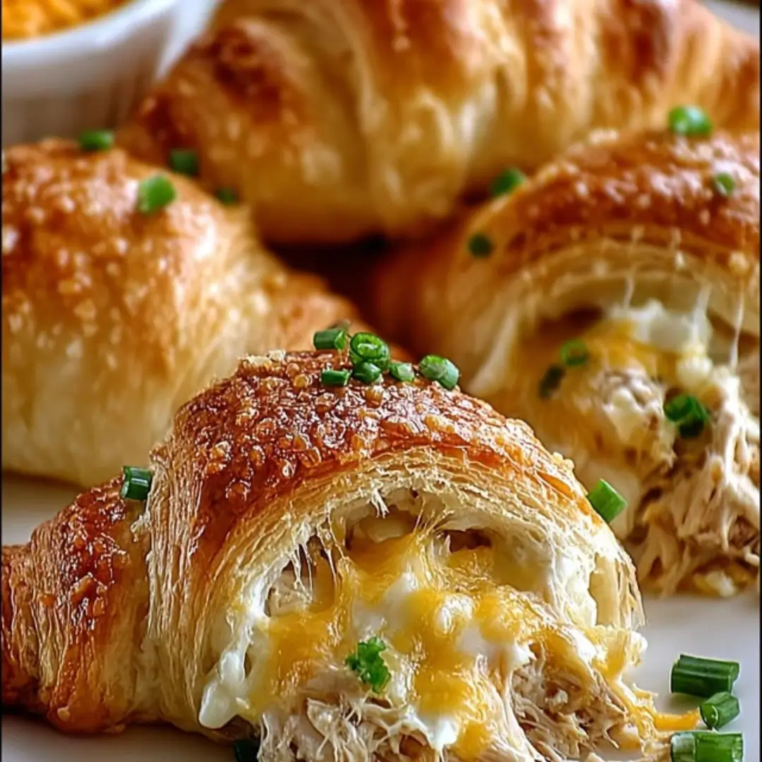 Close-up of four golden-brown chicken stuffed crescent rolls sprinkled with breadcrumbs on a parchment-lined baking sheet.