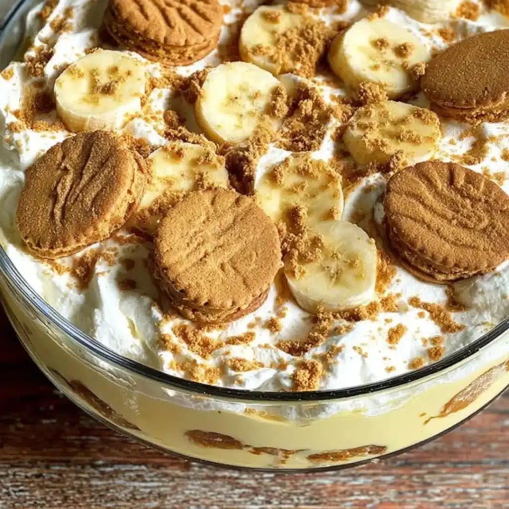 Biscoff Banana Pudding layered in a clear glass bowl, topped with whipped cream, sliced bananas, whole Biscoff cookies, and crushed cookie pieces.
