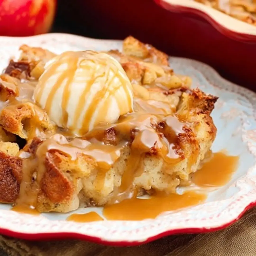 A warm slice of homemade Caramel Apple Bread Pudding topped with a scoop of melting vanilla ice cream and a generous drizzle of rich caramel sauce.
