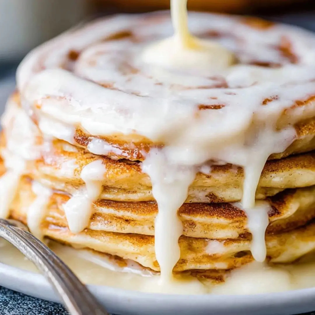 Stack of fluffy Cinnamon Roll Pancakes drizzled generously with a creamy white cream cheese glaze.