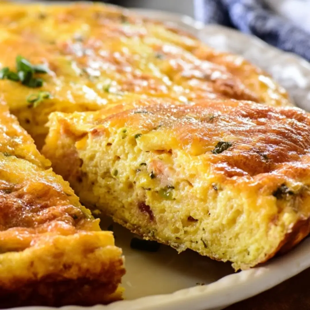 A fluffy, golden-yellow Denver Frittata sliced in a skillet, showing pieces of ham, green and red bell peppers, and melted cheddar cheese.