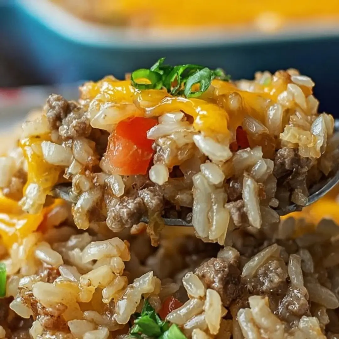 A close-up of a spoonful of cheesy hamburger rice casserole, garnished with chopped green onion, showing the cooked rice, ground beef, and melted cheddar cheese.
