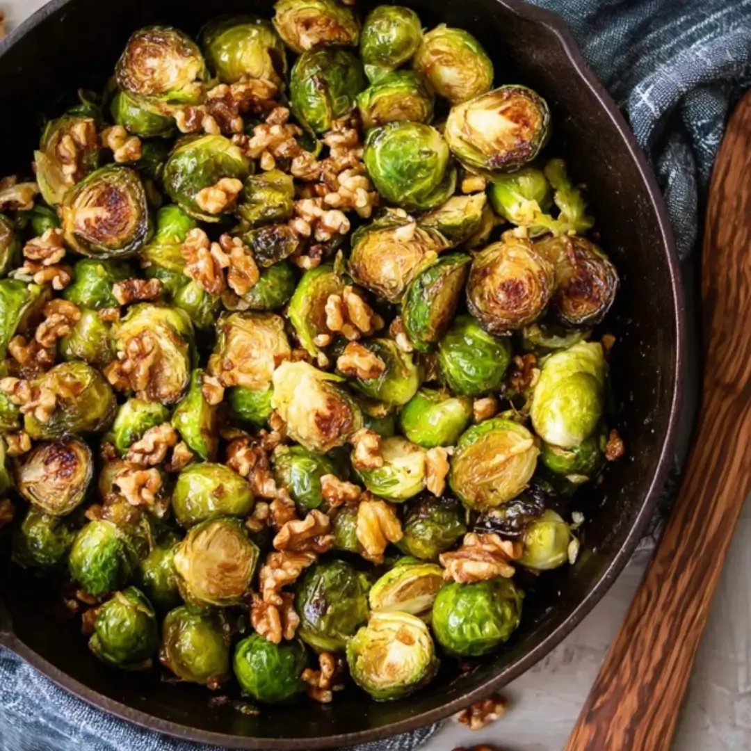 Roasted Brussels sprouts in a cast iron skillet, caramelized and tossed with whole walnuts, drizzled with a maple glaze.
