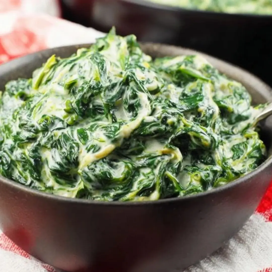 Creamed Spinach Recipe: A close-up shot of rich, dark green spinach coated in a thick, velvety white cream and Parmesan cheese sauce, served in a rustic brown bowl.