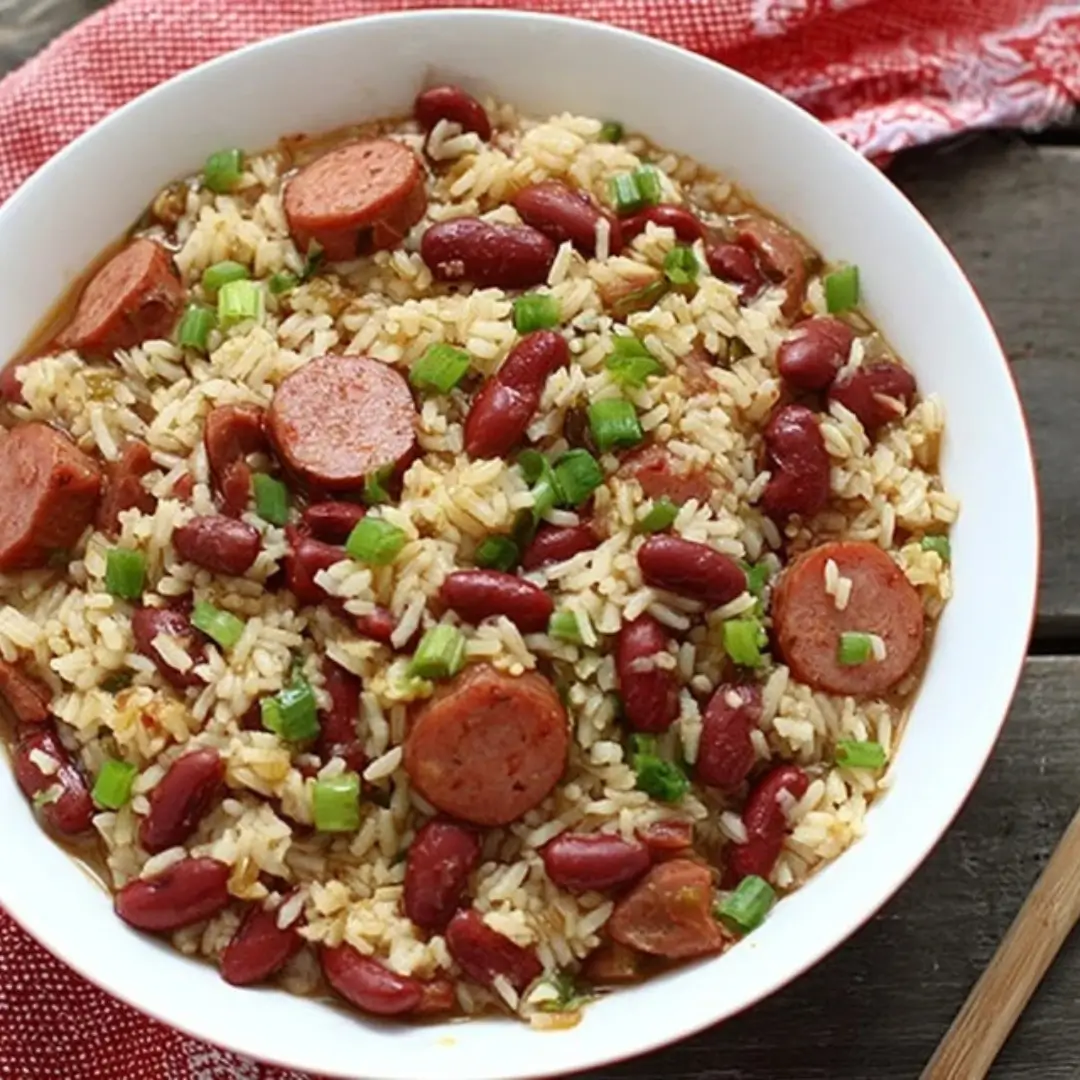 A white bowl filled with Easy One-Pot Red Beans and Rice, featuring red kidney beans, long-grain rice, and slices of cooked chicken sausage, garnished with chopped green onions.