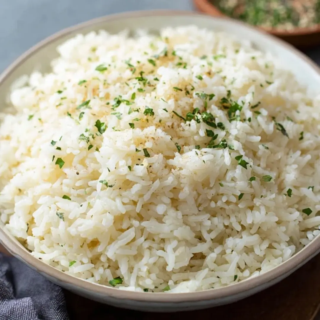 A close-up shot of a bowl filled with fluffy white Parmesan Garlic Butter Rice, garnished with fresh chopped parsley and a dusting of grated cheese.