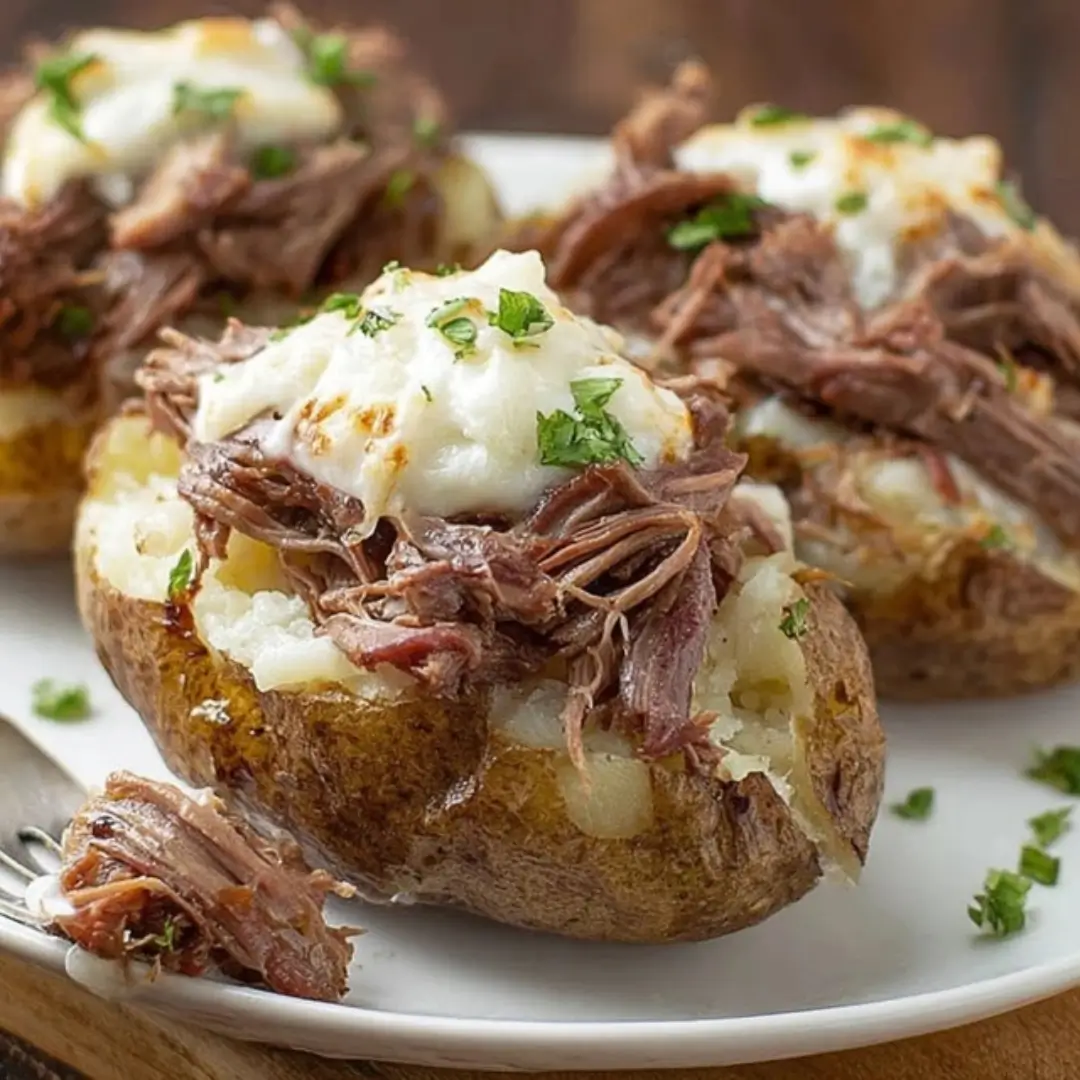 Pot Roast Stuffed Twice Baked Potatoes topped with shredded beef, melted mozzarella cheese, and fresh parsley, served on a white plate.