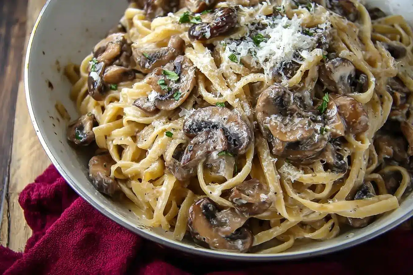A close-up of a pan of creamy mushroom pasta with fettuccine, garnished with grated parmesan cheese and fresh parsley.