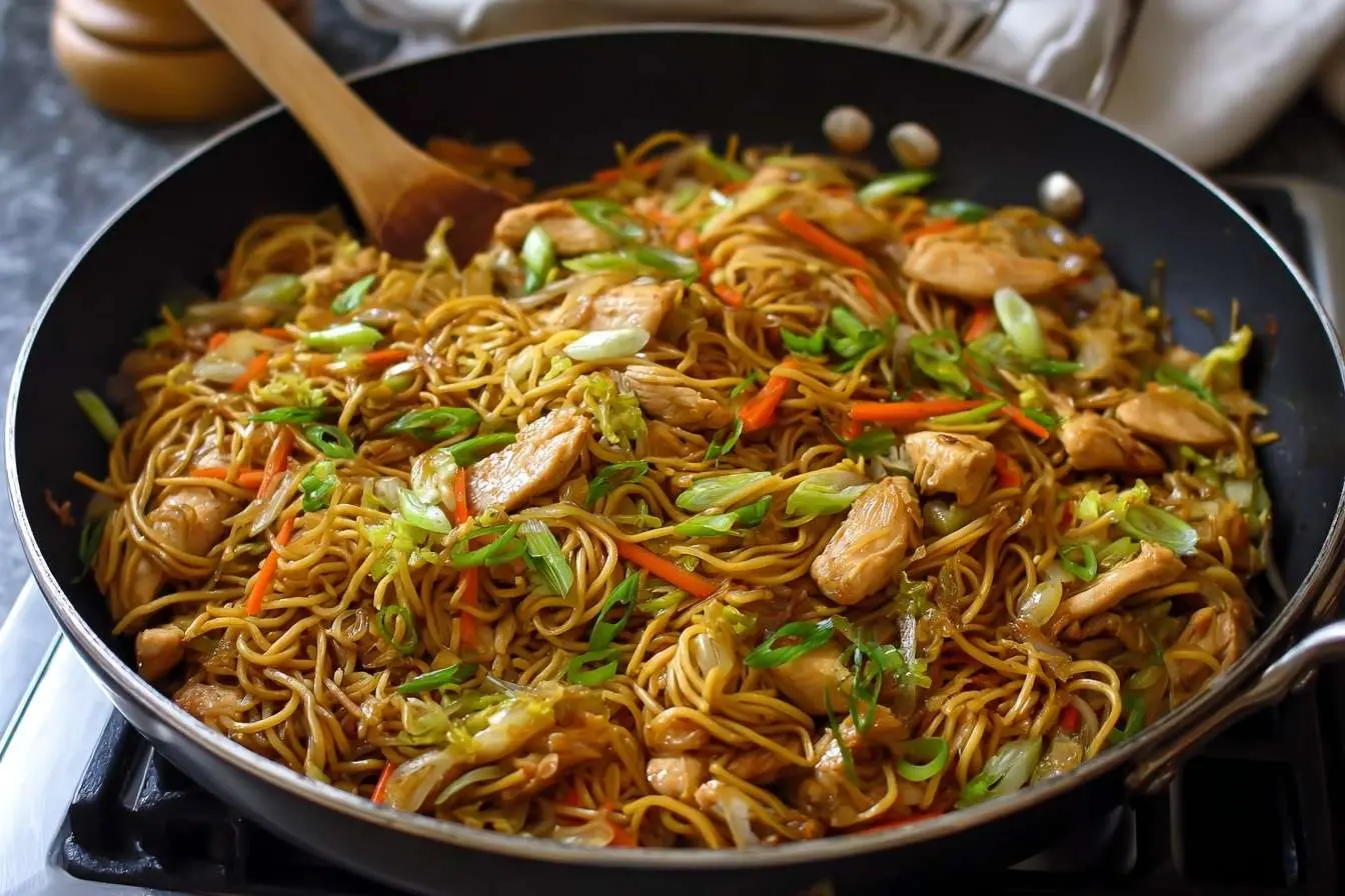 A large skillet filled with homemade Chicken Chow Mein, tossed with chicken, cabbage, carrots, and topped with green onions.