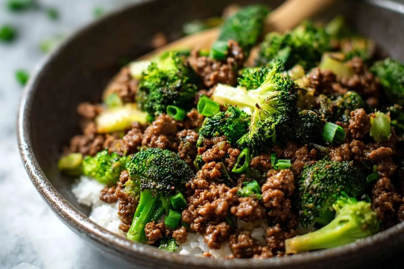 A close-up of a delicious ground beef and broccoli dish served over fluffy white rice in a dark ceramic bowl, garnished with scallions.