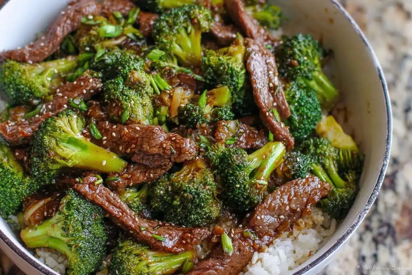 A close-up shot of a savory Beef and Broccoli stir-fry with sesame seeds and scallions, served over white rice in a bowl.