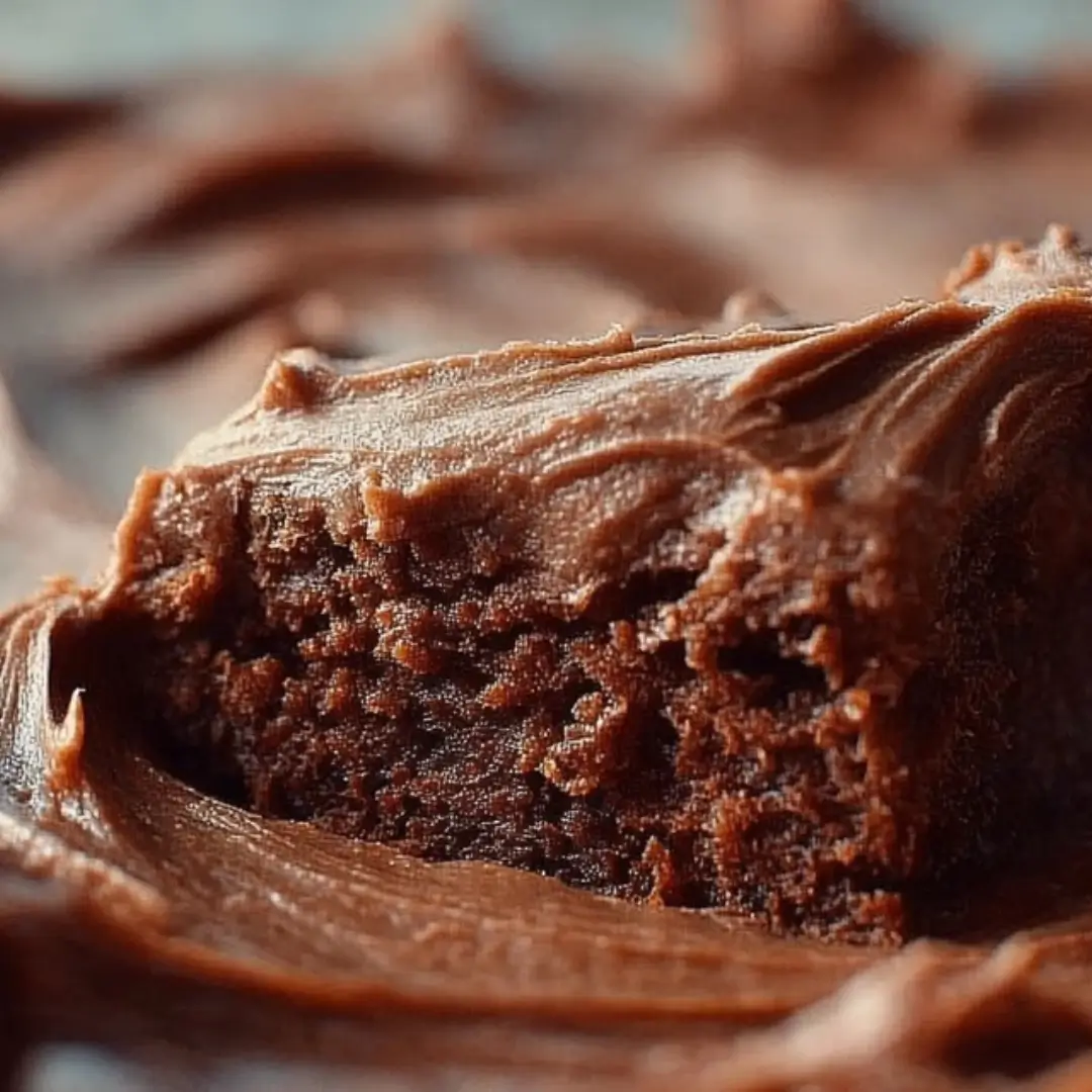 Close-up of a rich, fudgy brownie topped with a thick layer of swirled chocolate fudge frosting.