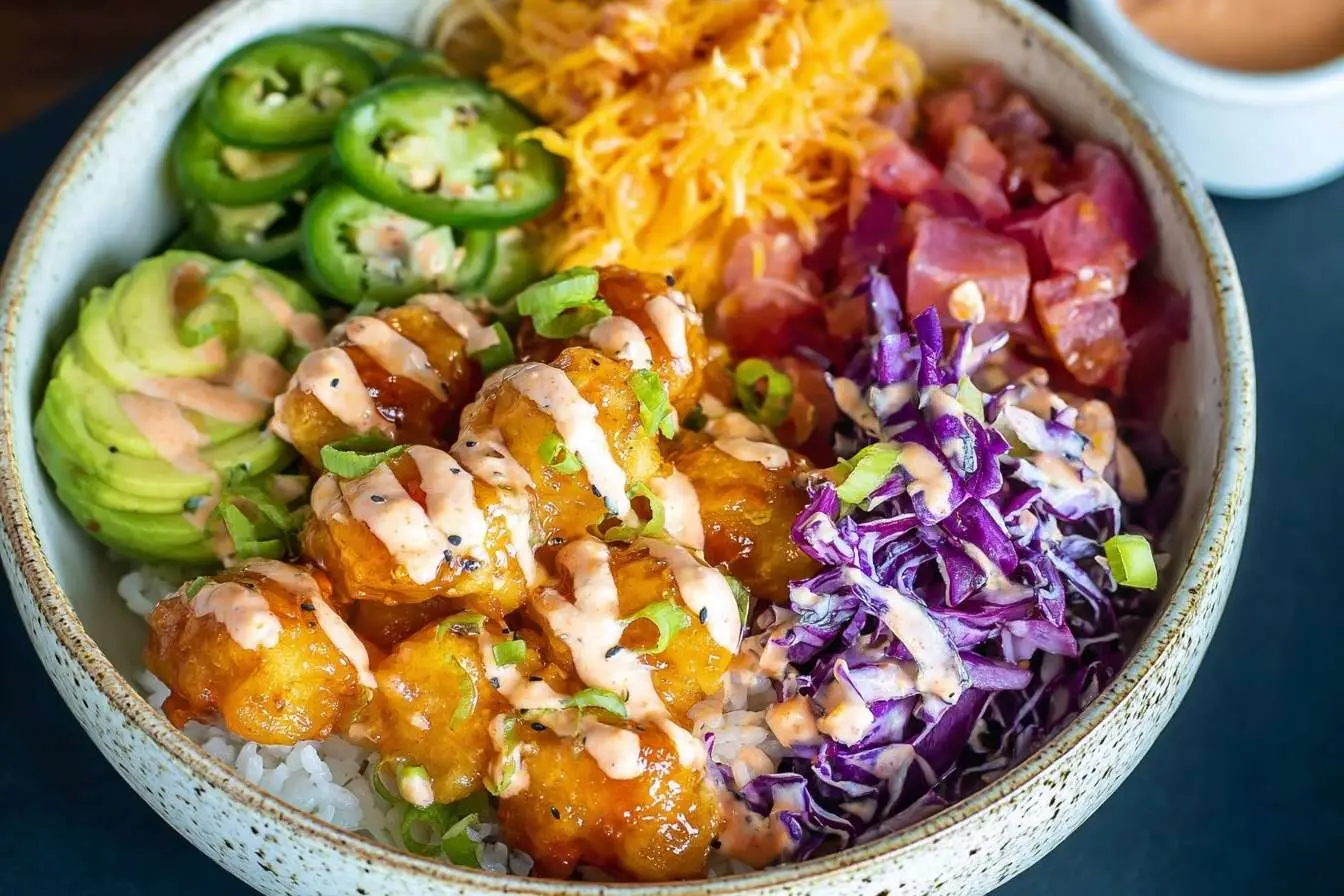 A colorful poke bowl recipe with crispy shrimp, ahi tuna, sliced avocado, and fresh toppings served on a bed of rice.