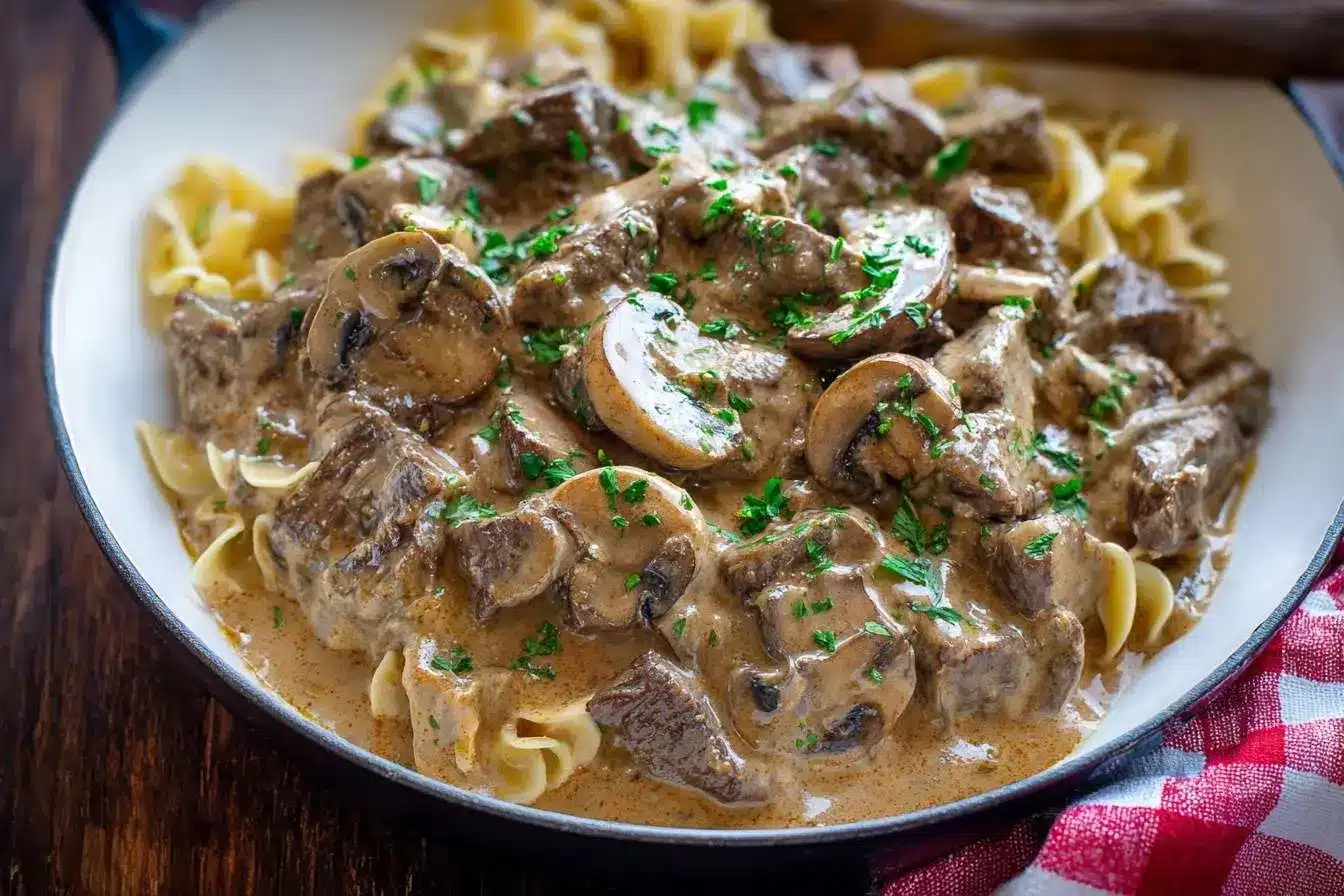 A close-up of creamy Beef Stroganoff with tender beef and mushrooms served over egg noodles in a white skillet.