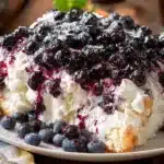 A slice of homemade {{ $('Fetch Recipe Data').first().json["Main Keyword"] }} topped with whipped cream, a rich blueberry sauce, and fresh blueberries.