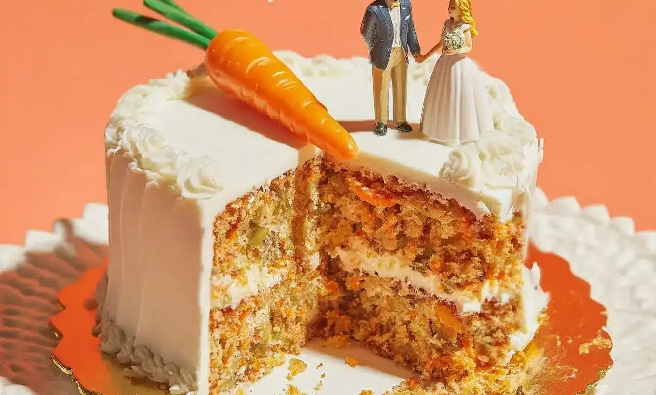 A beautiful two-layer carrot cake with a slice removed, made from a carrot cake recipe and topped with a bride and groom figurine.
