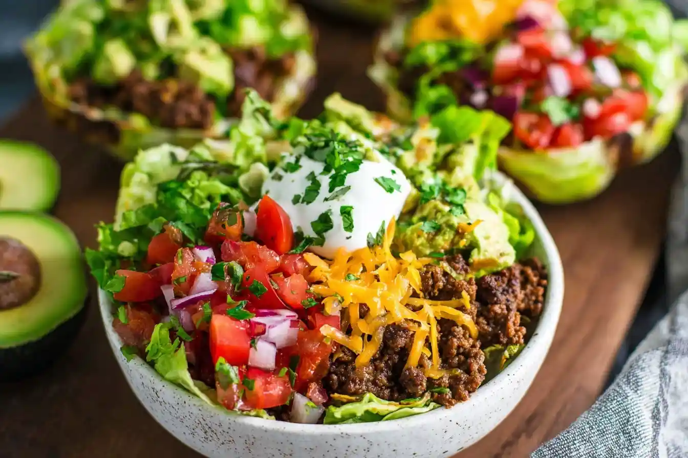 Close-up of a fresh taco salad bowl topped with beef, cheese, salsa, sour cream, and avocado.
