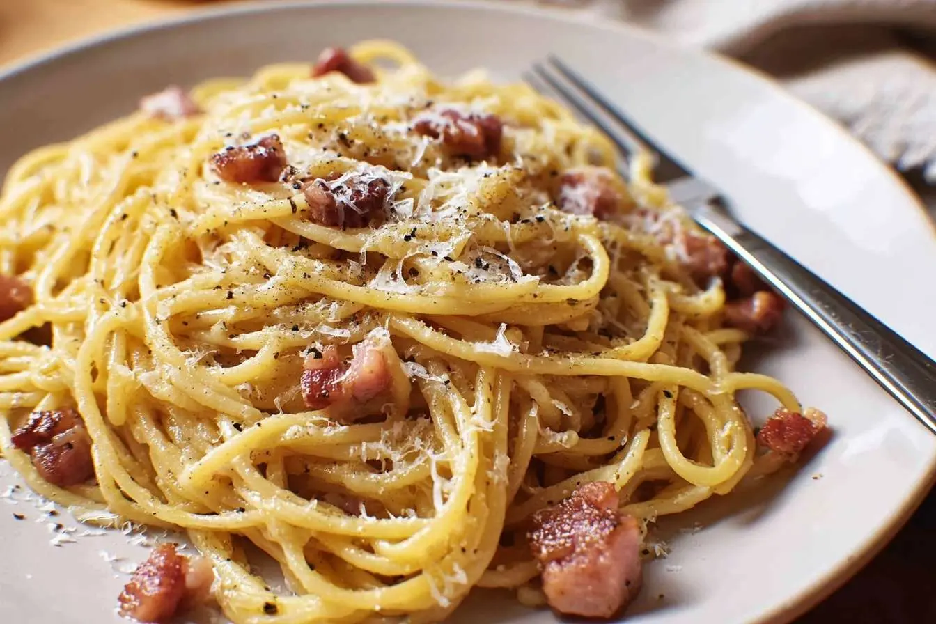 A close-up of a delicious plate of spaghetti carbonara, topped with crispy pancetta, cheese, and fresh black pepper.