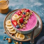 Vibrant pink smoothie bowl topped with fresh berries, sliced banana, and crunchy granola.