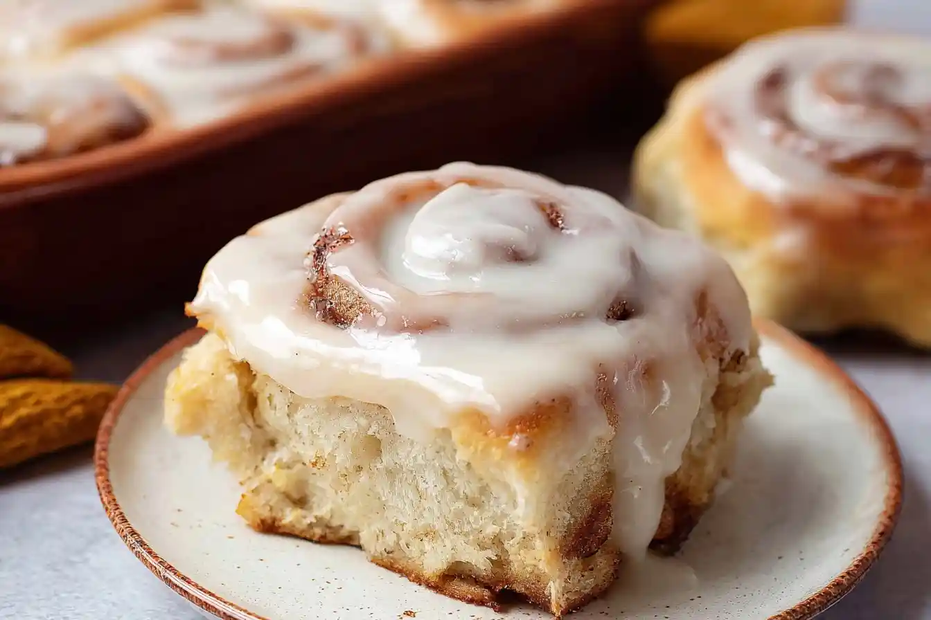 Close-up of a fluffy homemade cinnamon roll topped with thick white icing on a speckled ceramic plate.