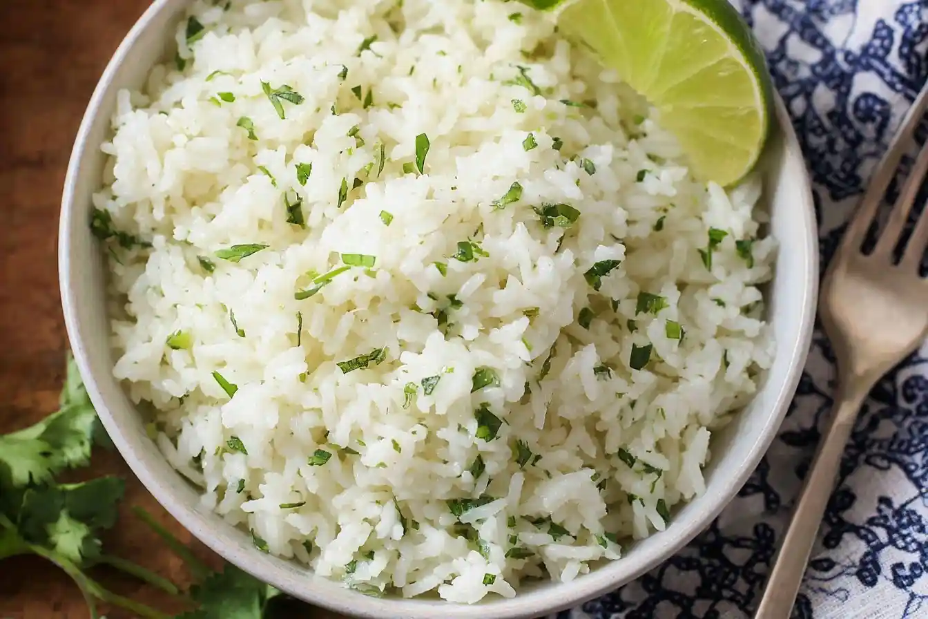 A bowl of fluffy cilantro lime rice garnished with a fresh lime wedge, next to a fork.