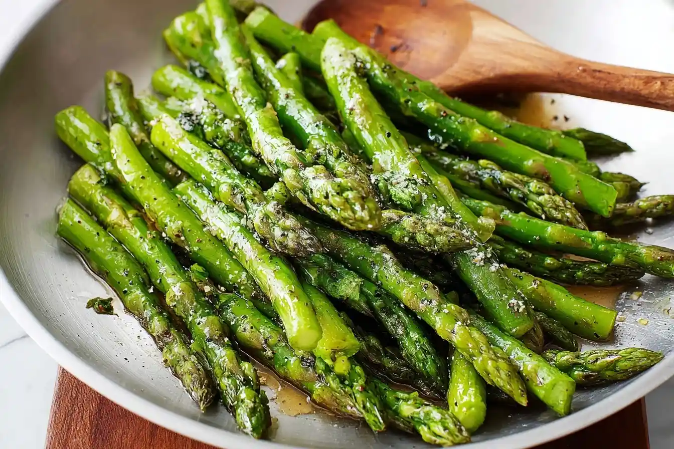 A silver skillet of fresh sauteed asparagus coated in oil and seasoned with salt and herbs.