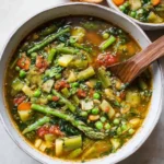 A vibrant bowl of {{ $('Fetch Recipe Data').first().json["Main Keyword"] }} featuring asparagus, peas, and a wooden spoon.